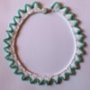 A knitted necklace with a crocheted, beaded edging in white and turquoise 