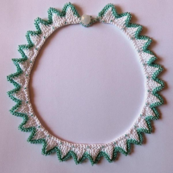 A knitted necklace with a crocheted, beaded edging in white and turquoise 