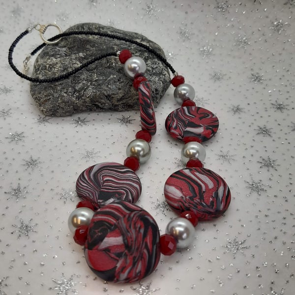 Disc shaped necklace in a red, black and silver swirl design