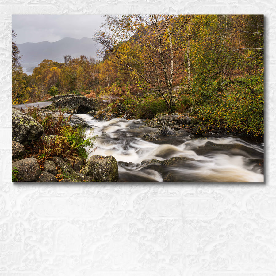 Autumn scene of a river rushing under arched Ashness bridge, Lake District.