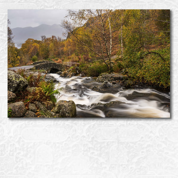 Autumn scene of a river rushing under arched Ashness bridge, Lake District.