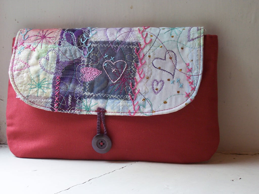 Soft fabric clutch bag with hand embroidered details in pink and lilac