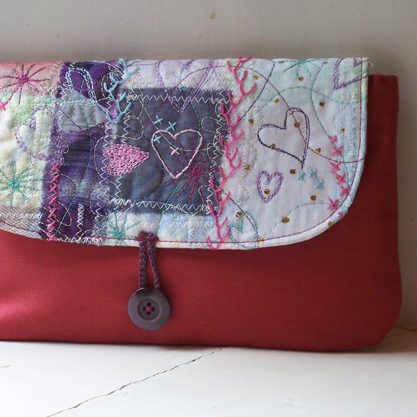 Soft fabric clutch bag with hand embroidered details in pink and lilac