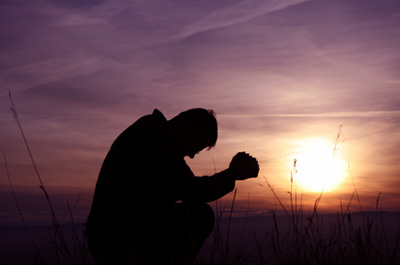 A man praying silhouetted in the sun.