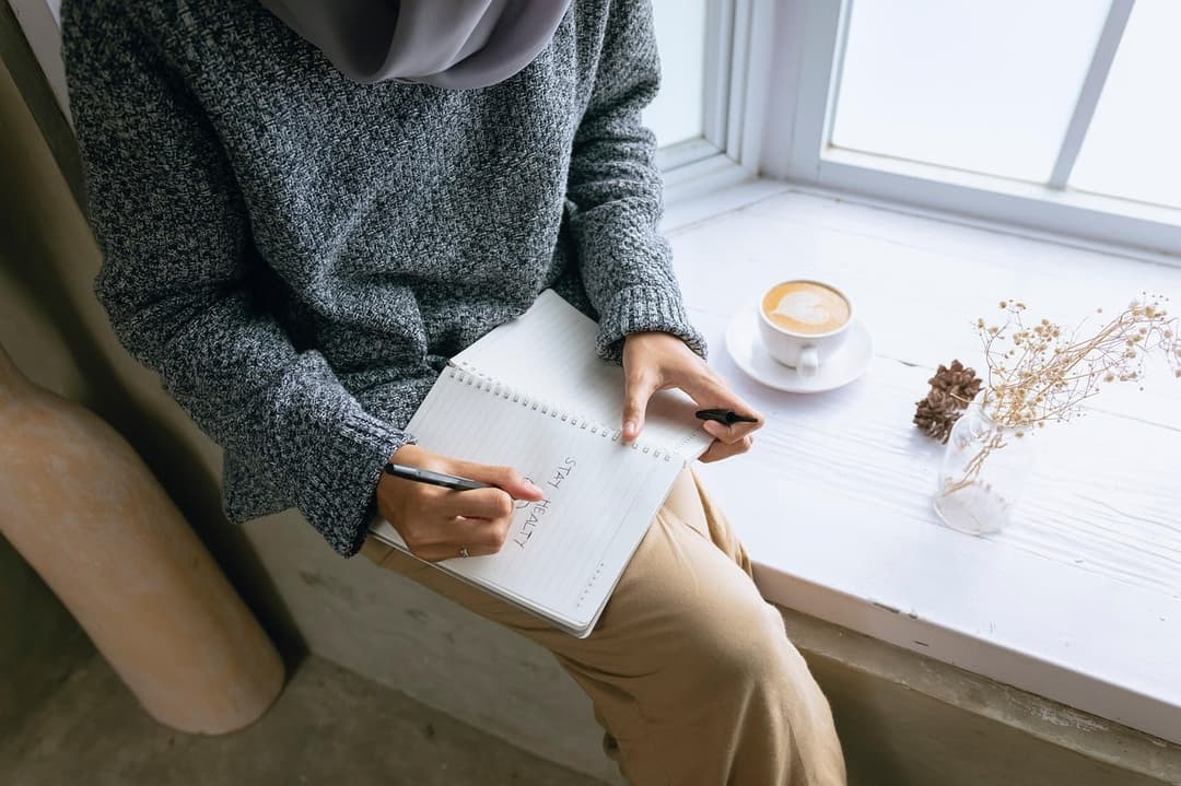 A woman writing in a notebook by a sunny window