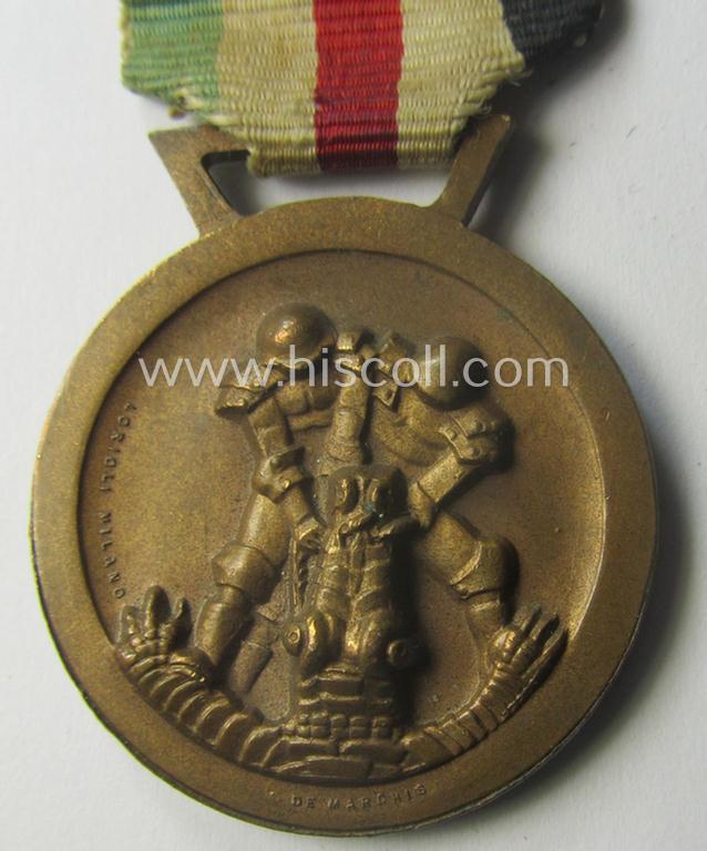 Golden-bronze-coloured- (and I deem 'Buntmetall'-based-) example of a: 'Deutsch-Italienische Feldzugsmedaille' (or: German-Italian campaign-medal) that comes mounted onto its (regular-sized) piece of original (and minimally faded!) ribbon