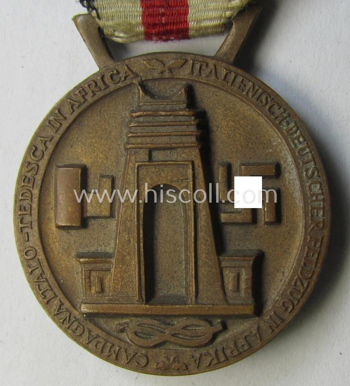 Attractive, golden-bronze-coloured- (and I deem 'Buntmetall'-based-) example of a: 'Deutsch-Italienische Feldzugsmedaille' (or: German-Italian campaign-medal) that comes mounted onto its (regular-sized) piece of original (albeit truly faded) ribb...