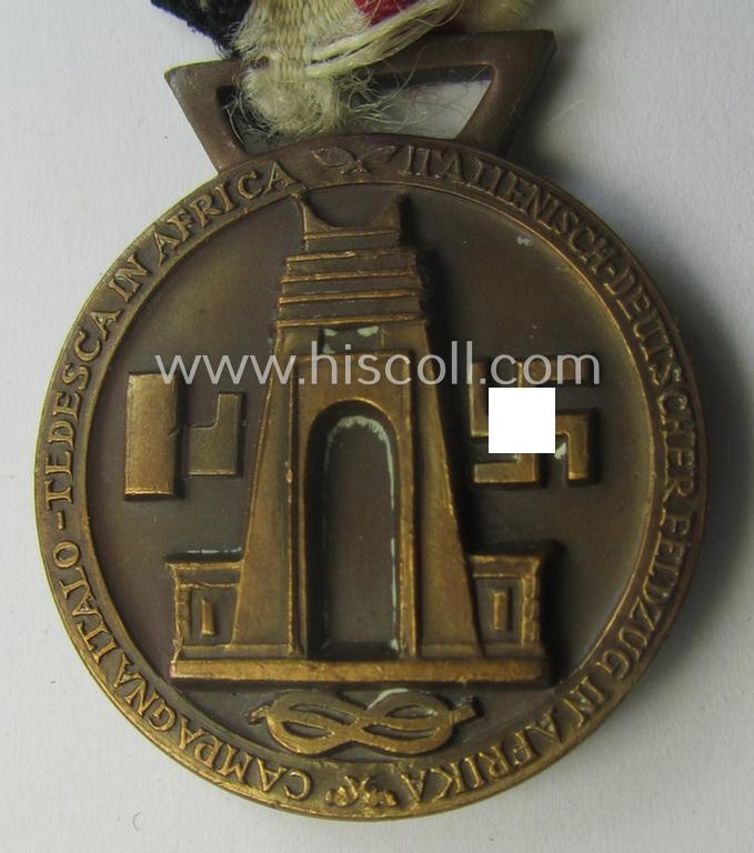 Golden-bronze-coloured- (and I deem 'Buntmetall'-based-) example of a: 'Deutsch-Italienische Feldzugsmedaille' (or: German-Italian campaign-medal) that comes mounted onto its (regular-sized) piece of original (and sun-faded!) ribbon