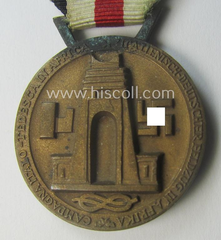 Golden-bronze-coloured- (and I deem 'Buntmetall'-based-) example of a: 'Deutsch-Italienische Feldzugsmedaille' (or: German-Italian campaign-medal) that comes mounted onto its (regular-sized) piece of original (and minimally faded!) ribbon