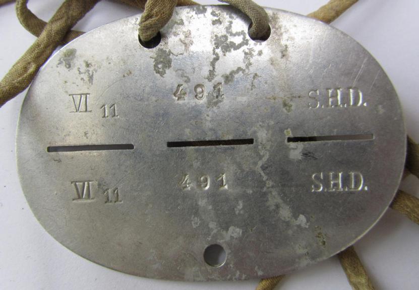 Aluminium-based, 'S.H.D.'- (ie. 'Sicherheits- u. Hilfsdienst'-) related ID-disc that comes mounted on its original cord as issued and/or worn, bearing the neatly stamped unit-signification that reads: 'VI 11 491 S.H.D.'