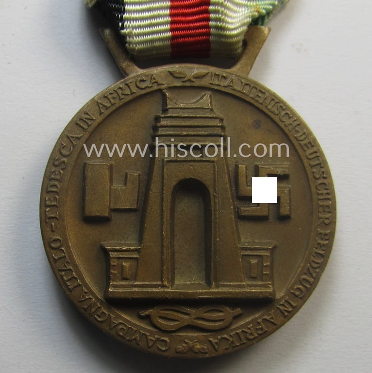 Golden-bronze-coloured- (and I deem 'Buntmetall'-based-) example of a: 'Deutsch-Italienische Feldzugsmedaille' (or: German-Italian campaign-medal) that comes mounted onto its (regular-sized) piece of original (and somewhat faded!) ribbon