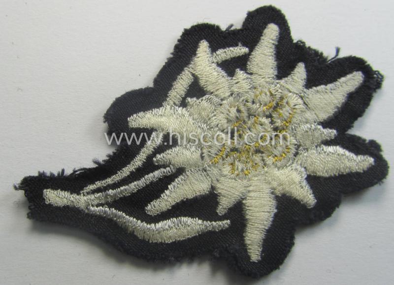 Waffen-SS-pattern, black-coloured M43-cap-insignia (ie. 'Mützenabzeichen') depicting an: 'Edelweiss'-flower as used by the various 'Gebirgsjäger'- (ie. mountain-troops-) related divisional-staff