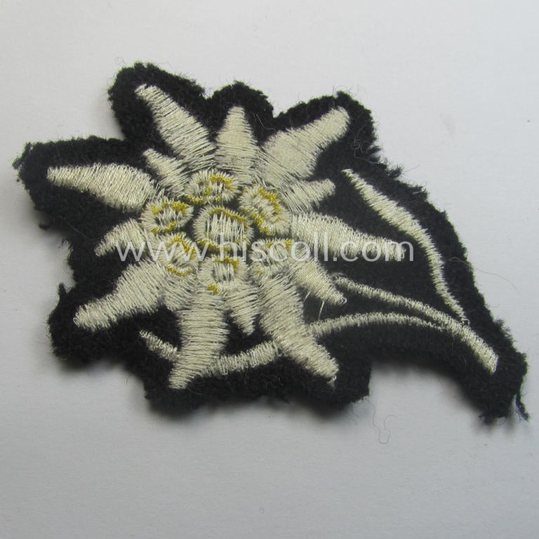 Waffen-SS-pattern, black-coloured M43-cap-insignia (ie. 'Mützenabzeichen') depicting an: 'Edelweiss'-flower as used by the various 'Gebirgsjäger'- (ie. mountain-troops-) related divisional-staff