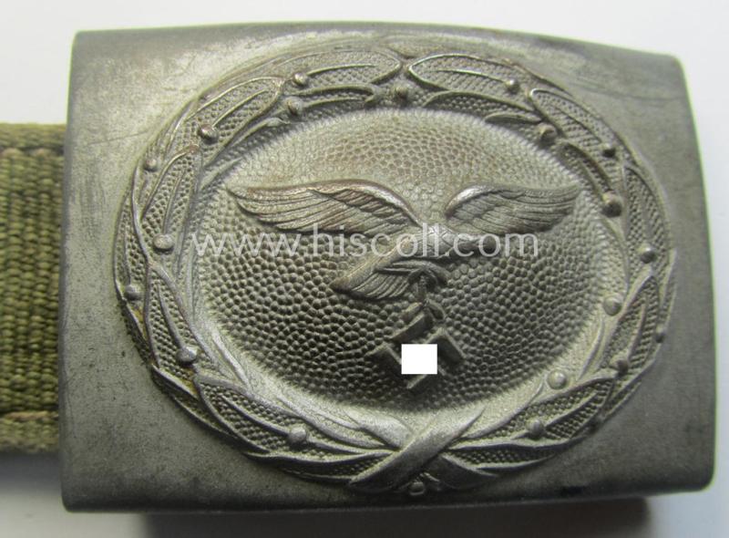 WH (Luftwaffe) 'tropical-issued' belt-buckle being a non-maker-marked, greyish-silver-coloured example that comes mounted onto its original, greenish-coloured- (and/or: 'webbing'-based-) tab