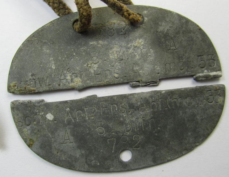 Zinc-based - albeit broken in two parts - WH (Heeres) 'Artillerie'-related ID-disc bearing the clearly stamped unit-designation that reads: 'Schw.Art.Abt.(mot.) 53 - 6 Bttr.' and that comes mounted onto its period cord as issued- and/or worn