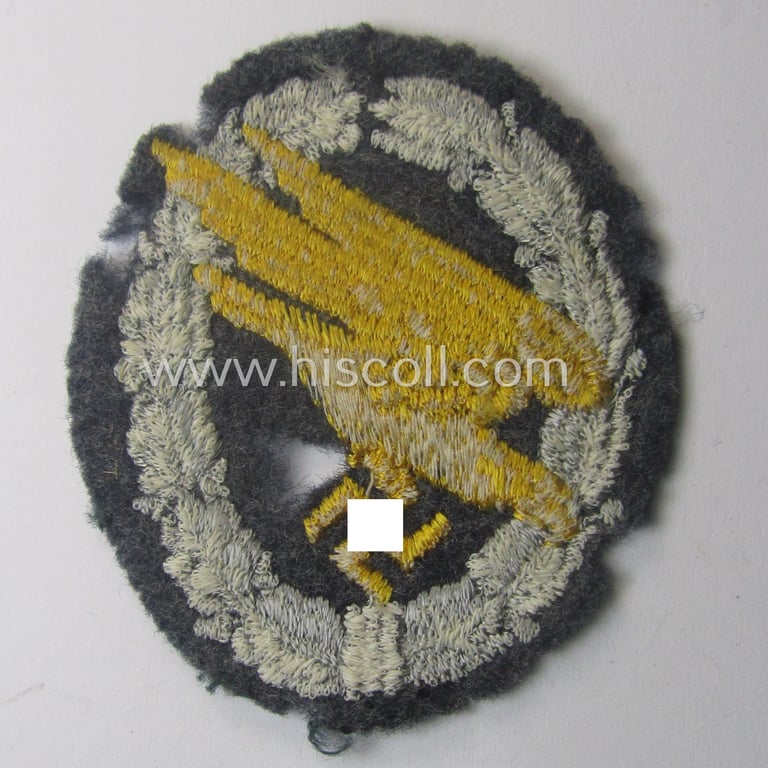 Truly used- and/or carefully tunic-removed, WH (Luftwaffe) 'Fallschirmschützen-Abzeichen in Stoff' (or: cloth-based paratroopers'-jump-badge) being a nicely machine-embroidered 'relic' specimen that comes in a clearly used- ie. worn, condition