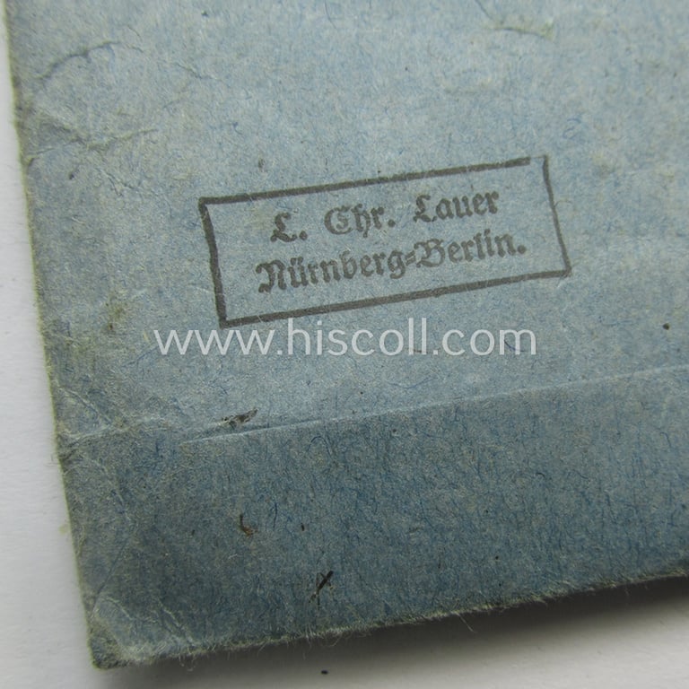 Matching 'EK II. Klasse'-set comprising of a non-maker-marked specimen that comes with its ribbon (ie. 'Bandabschnitt') and 'Zellstoff'-based pouch as was produced by the company: 'L.Chr. Lauer' (ie. 'Hersteller 14')