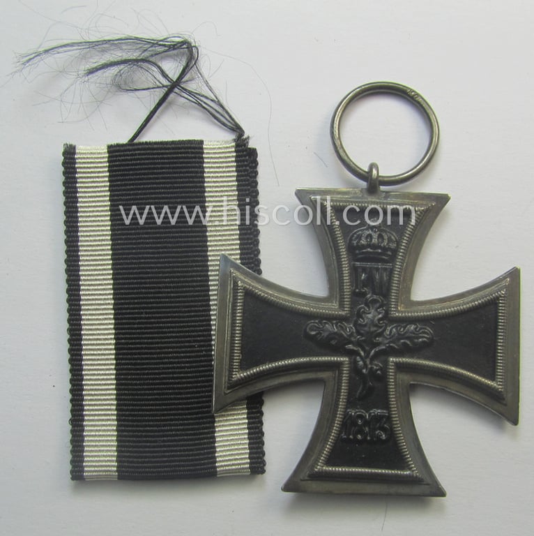 WWI-period: 'Eisernes Kreuz II. Klasse' (or: iron cross second class) being a maker- (ie. 'KO'-) marked example that comes together with its (minimally) confectioned piece of ribbon (ie. 'Bandabschnitt')