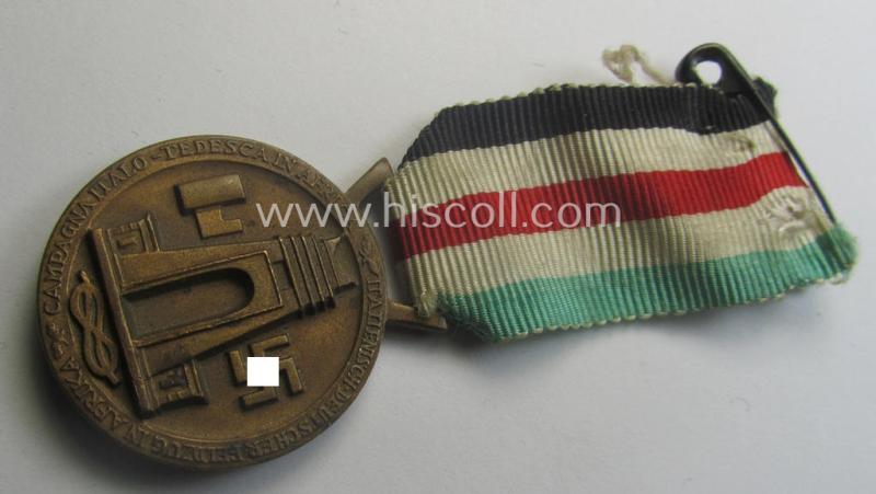 Golden-bronze-coloured- (and I deem 'Buntmetall'-based-) example of a: 'Deutsch-Italienische Feldzugsmedaille' (or: German-Italian campaign-medal) that comes mounted onto its (regular-sized) piece of original (and minimally faded!) ribbon