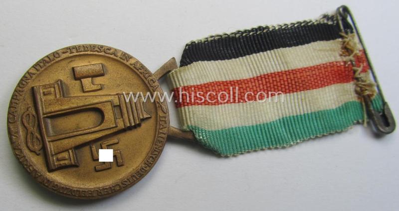 Golden-bronze-coloured- (and I deem 'Buntmetall'-based-) example of a: 'Deutsch-Italienische Feldzugsmedaille' (or: German-Italian campaign-medal) that comes mounted onto its (regular-sized) piece of original (and minimally faded!) ribbon