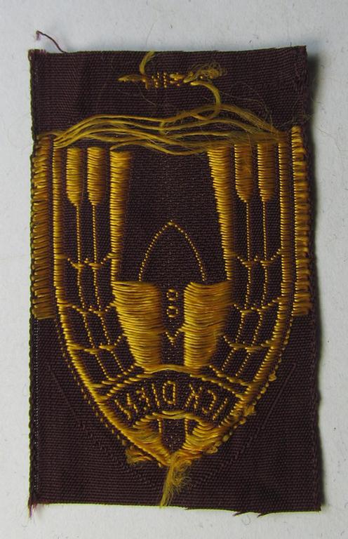 Neat - and nicely 'BeVo-woven'-like - Dutch WWII-period, labour service ie. 'Nederlandse Arbeidsdienst' (or: NAD) cap-badge entitled: 'Ick Dien' and that comes in a 'virtually mint- ie. unissued', condition