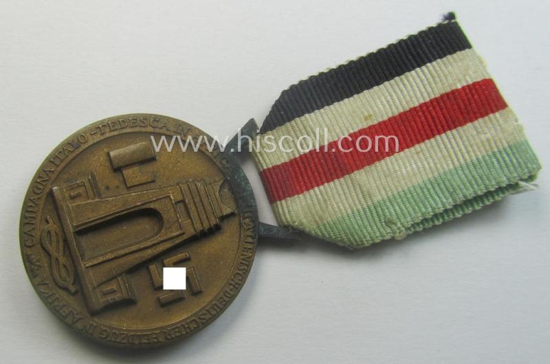 Golden-bronze-coloured- (and I deem 'Buntmetall'-based-) example of a: 'Deutsch-Italienische Feldzugsmedaille' (or: German-Italian campaign-medal) that comes mounted onto its (regular-sized) piece of original (and minimally faded!) ribbon