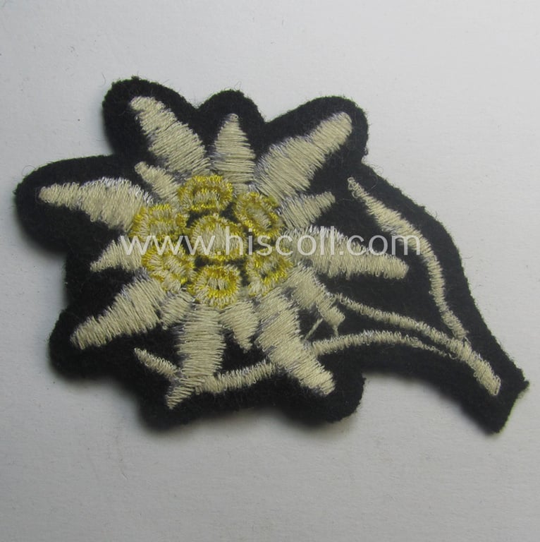 Waffen-SS-pattern, black-coloured M43-cap-insignia (ie. 'Mützenabzeichen') depicting an: 'Edelweiss'-flower as used by the various 'Gebirgsjäger'- (ie. mountain-troops-) related divisional-staff