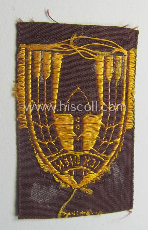 Neat - and nicely 'BeVo-woven'-like - Dutch WWII-period, labour service ie. 'Nederlandse Arbeidsdienst' (or: NAD) cap-badge entitled: 'Ick Dien' and that comes in a 'virtually mint- ie. unissued', condition