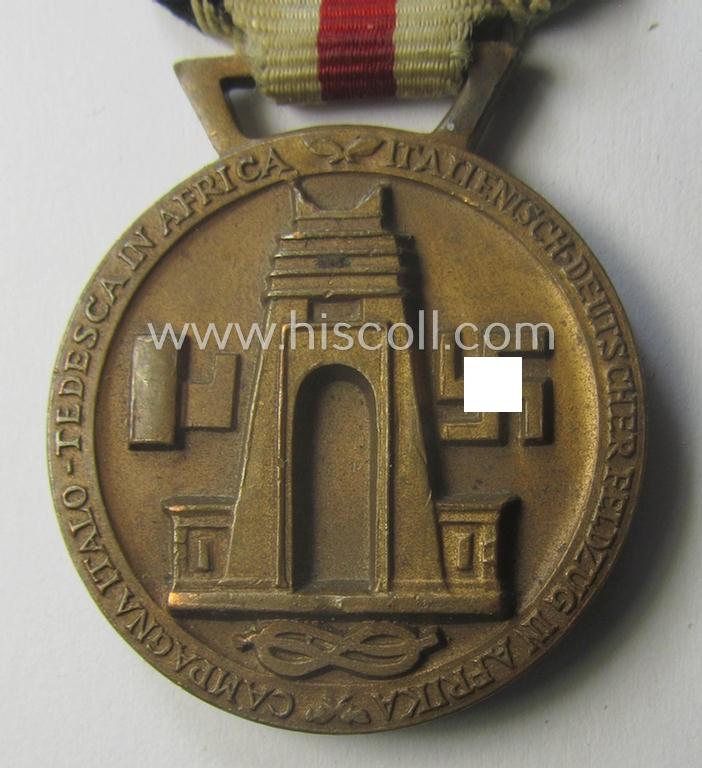 Golden-bronze-coloured- (and I deem 'Buntmetall'-based-) example of a: 'Deutsch-Italienische Feldzugsmedaille' (or: German-Italian campaign-medal) that comes mounted onto its (regular-sized) piece of original (and minimally faded!) ribbon
