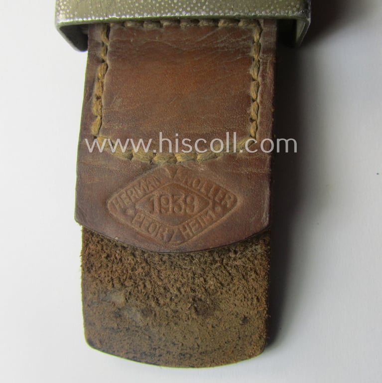 WH (Heeres) 'standard-pattern', field-grey-toned- and aluminium-based belt-buckle being a maker- (ie. 'Hermann Knoller - Pforzheim'-) marked- and/or: '1939'-dated example that comes mounted onto its leather-based tab