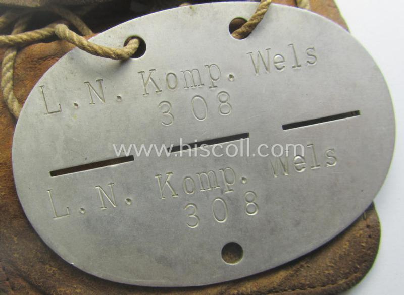 Aluminium-based, WH (Luftwaffe) ie. 'Luftnachrichten'-related ID-disc (ie. 'Erkennungsmarke') bearing the stamped unit-designation that reads: 'L.N. Komp. Wels' and that comes stored in its period (leather-based) pouch
