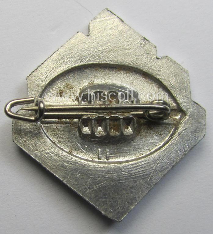 Silverish-coloured and aluminium-based, N.S.D.A.P.-related lapel-pin (ie. 'Mitgliedsabzeichen') being a commemorative example that shows an (enamelled and three-dimensional!) swastika surrounded by the text: 'Nationale Solidarität'