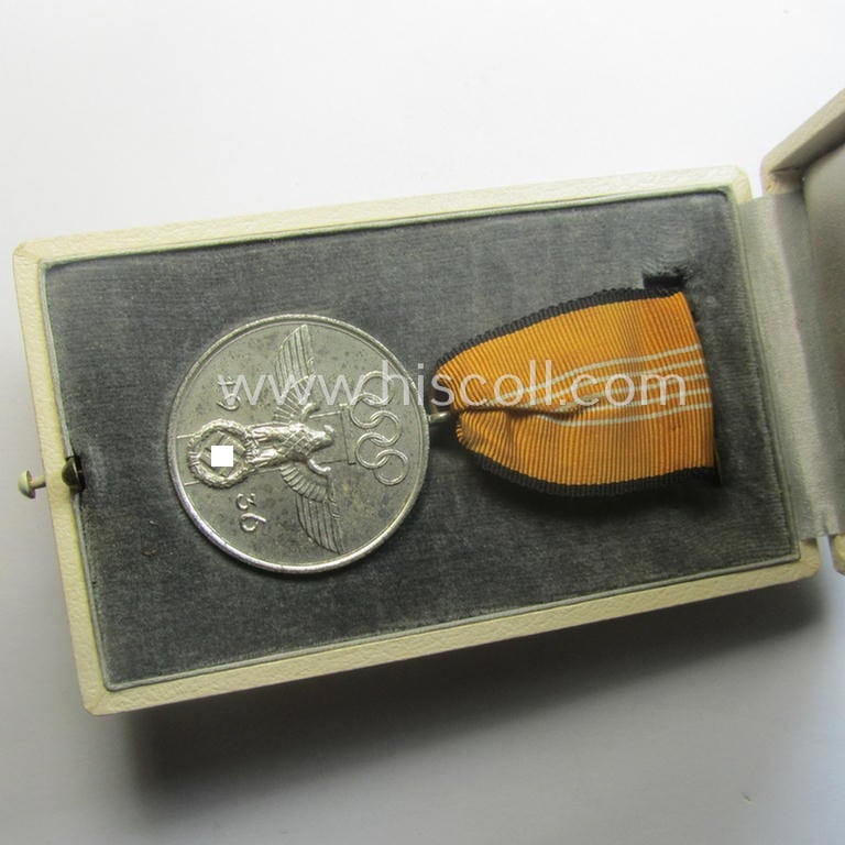 'Deutsche Olympia-Erinnerungsmedaille 1936' being a non-maker-marked example that comes mounted onto its original ribbon (ie. 'Bandabschnitt') and that comes stored in its typical, beige-white-coloured etui