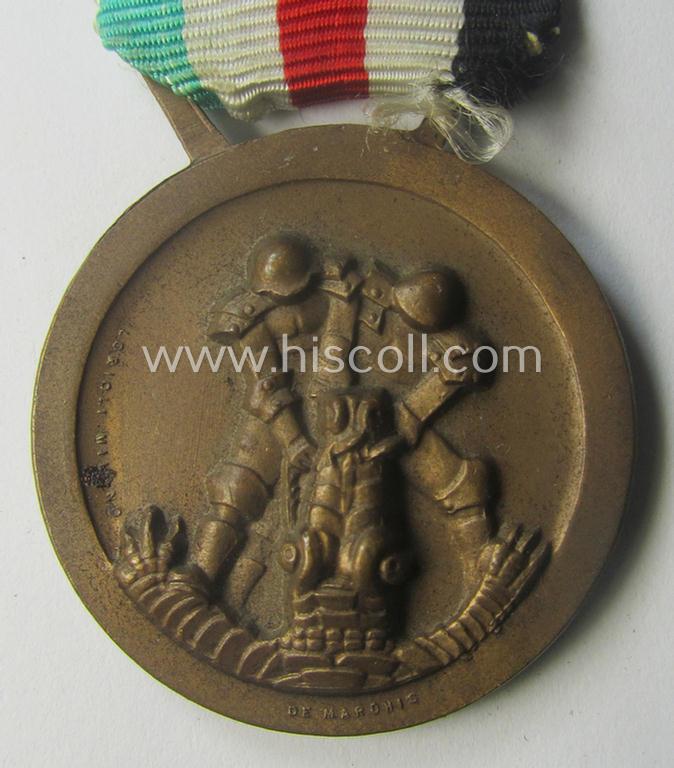 Golden-bronze-coloured- (and I deem 'Buntmetall'-based-) example of a: 'Deutsch-Italienische Feldzugsmedaille' (or: German-Italian campaign-medal) that comes mounted onto its (regular-sized) piece of original (and hardly faded!) ribbon