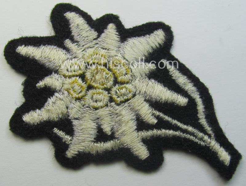 Waffen-SS-pattern, black-coloured M43-cap-insignia (ie. 'Mützenabzeichen') depicting an: 'Edelweiss'-flower as used by the various 'Gebirgsjäger'- (ie. mountain-troops-) related divisional-staff