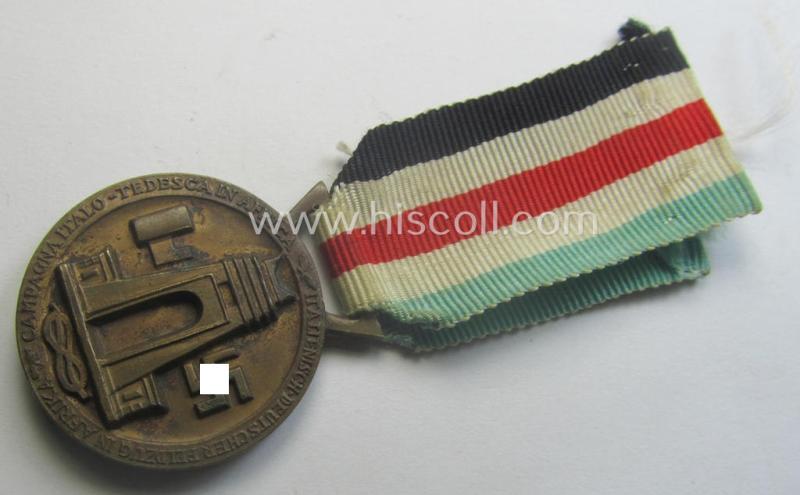 Golden-bronze-coloured- (and I deem 'Buntmetall'-based-) example of a: 'Deutsch-Italienische Feldzugsmedaille' (or: German-Italian campaign-medal) that comes mounted onto its (regular-sized) piece of original (and hardly faded!) ribbon