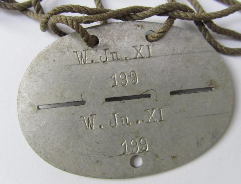 Neat, aluminium-based-, WH (Heeres-) ie. 'Wehrkreis'-related ID-disc, bearing the clearly stamped unit-designation: 'W.Jn.XI' and that comes mounted on its period-attached cord as issued and/or worn