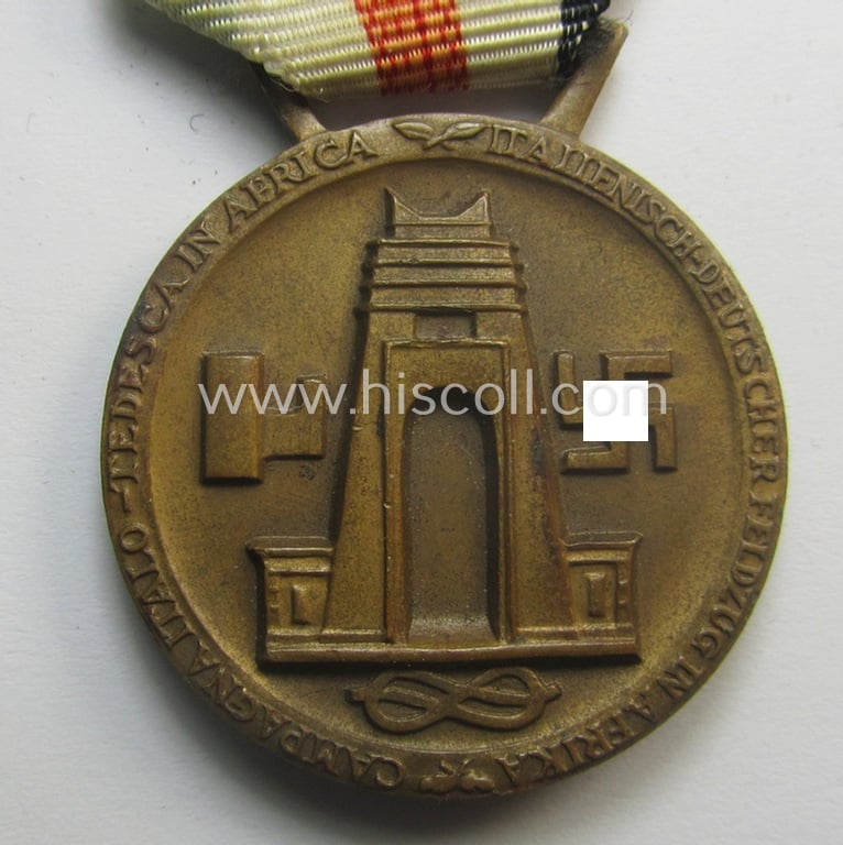 Golden-bronze-coloured- (and I deem 'Buntmetall'-based-) example of a: 'Deutsch-Italienische Feldzugsmedaille' (or: German-Italian campaign-medal) that comes mounted onto its (regular-sized) piece of original (and somewhat faded!) ribbon