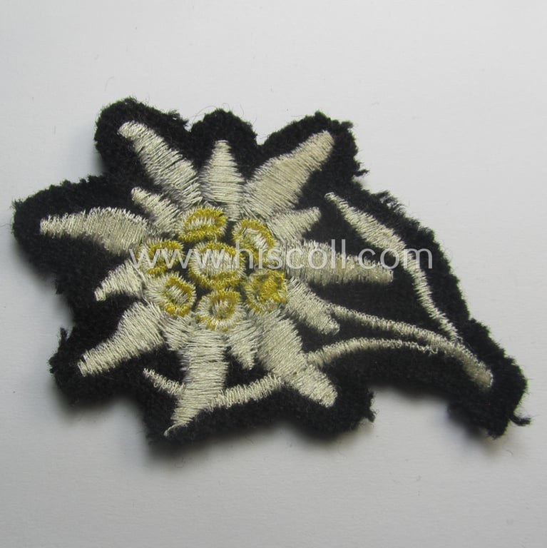 Waffen-SS-pattern, black-coloured M43-cap-insignia (ie. 'Mützenabzeichen') depicting an: 'Edelweiss'-flower as used by the various 'Gebirgsjäger'- (ie. mountain-troops-) related divisional-staff