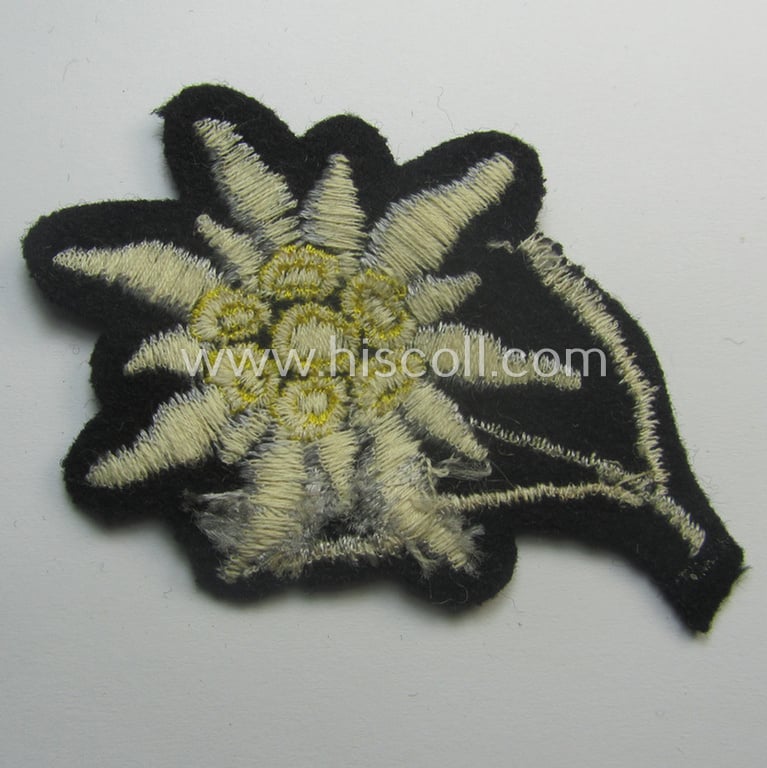 Waffen-SS-pattern, black-coloured M43-cap-insignia (ie. 'Mützenabzeichen') depicting an: 'Edelweiss'-flower as used by the various 'Gebirgsjäger'- (ie. mountain-troops-) related divisional-staff