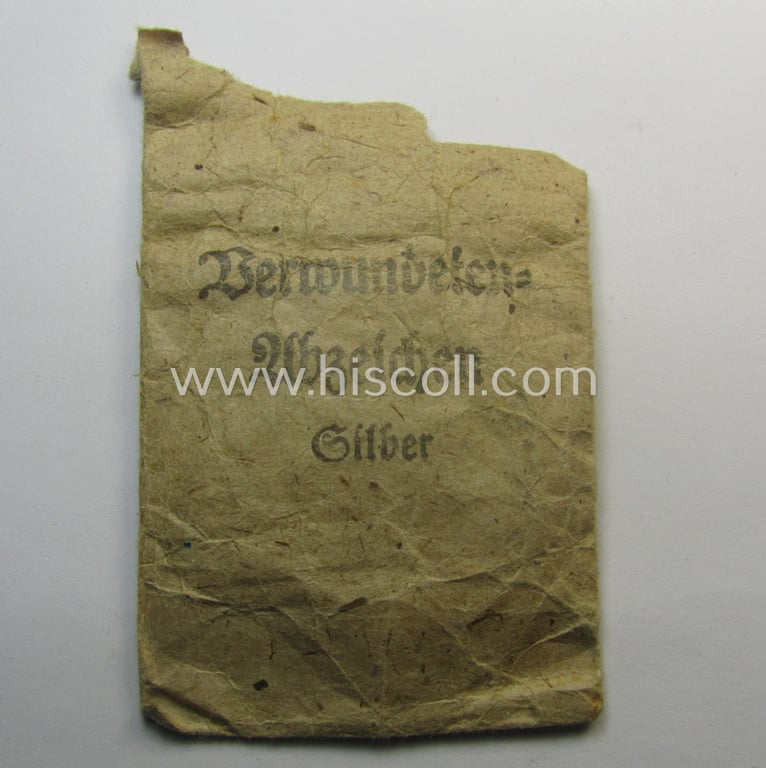 Unusual, silver-class wound-badge (or: 'Verwundeten-Abzeichen in Siber') being a maker- (ie. '127'-) marked example that comes stored in its original (damaged), carton-based pouch by the maker (ie. 'Hersteller'): 'Moriz Hausch A.-G.'