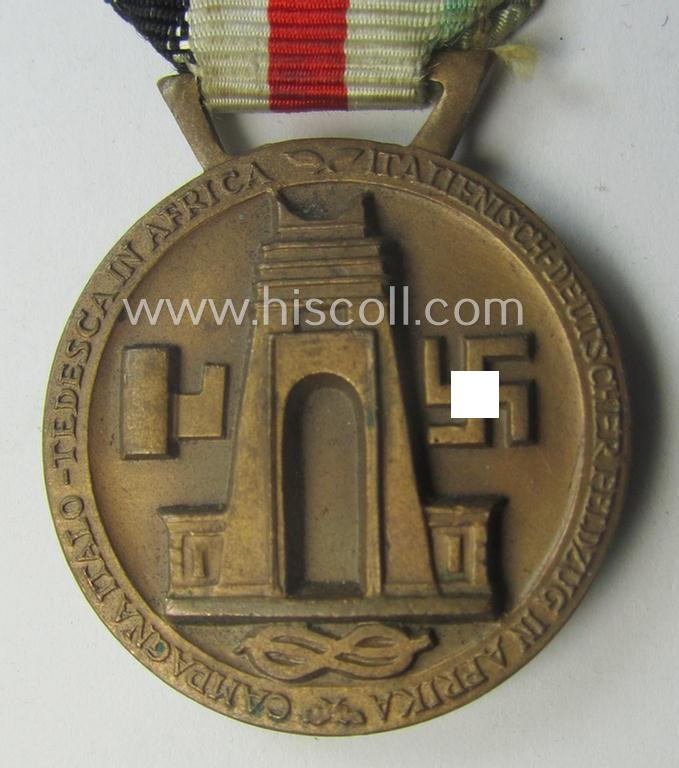 Golden-bronze-coloured- (and I deem 'Buntmetall'-based-) example of a: 'Deutsch-Italienische Feldzugsmedaille' (or: German-Italian campaign-medal) that comes mounted onto its (regular-sized) piece of original (and minimally faded!) ribbon