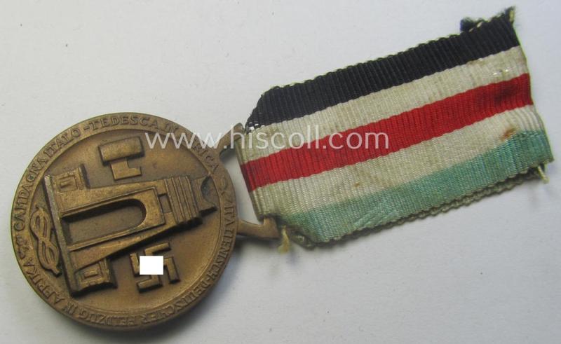 Golden-bronze-coloured- (and I deem 'Buntmetall'-based-) example of a: 'Deutsch-Italienische Feldzugsmedaille' (or: German-Italian campaign-medal) that comes mounted onto its (regular-sized) piece of original (and minimally faded!) ribbon