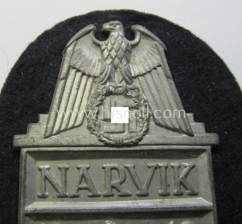 Superb - and scarcely encountered! - WH (KM) 'Narvik'-campaign-shield being a detailed example as executed in ('migriertes') golden-toned zinc- (ie. 'Feinzink') and that comes in an issued- (albeit I deem never worn- nor tunic-attached-), condi...