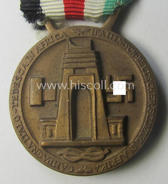 Golden-bronze-coloured- (and I deem 'Buntmetall'-based-) example of a: 'Deutsch-Italienische Feldzugsmedaille' (or: German-Italian campaign-medal) that comes mounted onto its (regular-sized) piece of original (and hardly faded!) ribbon