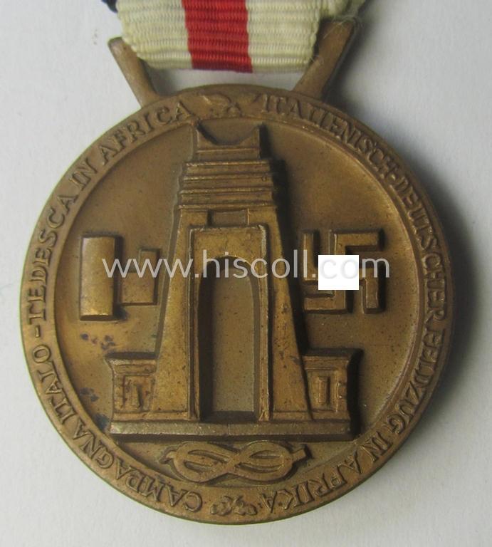 Golden-bronze-coloured- (and I deem 'Buntmetall'-based-) example of a: 'Deutsch-Italienische Feldzugsmedaille' (or: German-Italian campaign-medal) that comes mounted onto its (regular-sized) piece of original (and somewhat faded!) ribbon