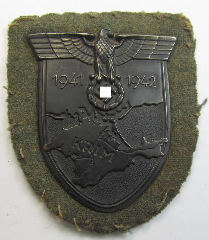 Attractive, WH (Heeres o. Waffen-SS) 'Krim'-campaign-shield that comes mounted onto its original, field-grey-coloured 'backing' and that comes in an issued-, moderately worn and/or carefully tunic-removed-, condition