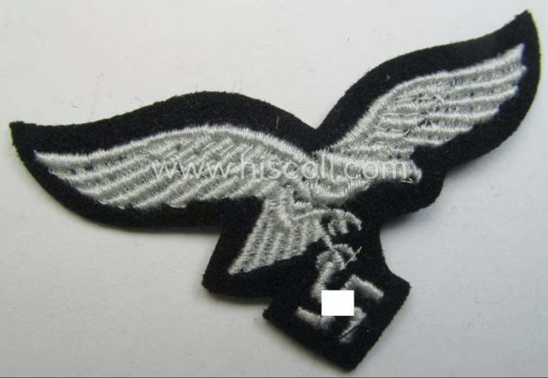 WH (Luftwaffe) cap-eagle (being a 'standard-issue'-pattern example that is executed onto a black-coloured background and that was as such intended for usage on the black-coloured work- ie. 'HG'-related side-caps ie. 'Schiffchen')