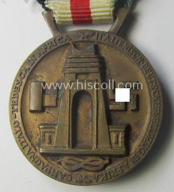 Golden-bronze-coloured- (and I deem 'Buntmetall'-based-) example of a: 'Deutsch-Italienische Feldzugsmedaille' (or: German-Italian campaign-medal) that comes mounted onto its (regular-sized) piece of original (and hardly faded!) ribbon