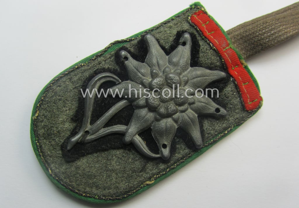 Never before seen, WH 'Gebirgsjäger'-related item: a semi-official, commemorative-talisman or: 'Url' that is privately-constructed from a (cut-off) shoulderstrap and zinc-based: 'Edelweiss'-M43 cap-badge